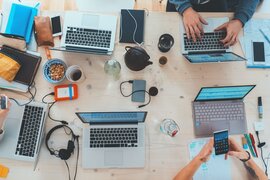 Laptops, Smartphones, Powerbanks, Notizbücher, Zettel, Stifte und Getränke, die auf einem Tisch stehen.