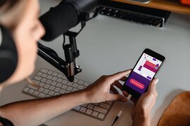 Eine Person, die in ein Mikrofon spricht und ein Smartphone in den Händen hält.