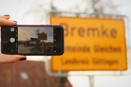 eine Frau, die ein Smartphone in der Hand hält, macht ein Foto vom Bremke Ortsschild
