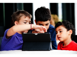 Kinder, die ein Tablet nutzen, welches vor ihnen auf einem Tisch steht.