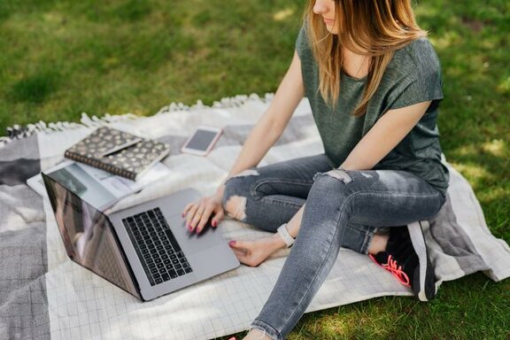 Eine sitzende Person, die einen Laptop vor sich stehen hat, auf dem sie tippt.