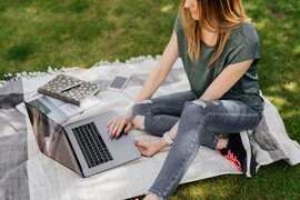 Eine sitzende Person, die einen Laptop vor sich stehen hat, auf dem sie tippt.