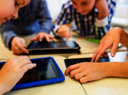Kinder, die an einem Tisch sitzen und mit Tablets beschäftigt sind.
