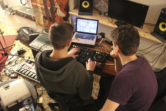 Zwei Menschen, die vor einem Laptop und einer Musikanlage sitzen.