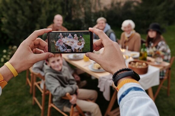 Eine Person, die mit einem Smartphone Menschen fotografiert, die an einem Tisch sitzen.