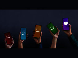 Hände, die Smartphones nach oben halten, auf denen traurige, unzufriedene sowie lachende Smilieys zu sehen sind.