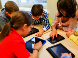 Kinder, die an Tischen sitzen, auf denen Tablets liegen.