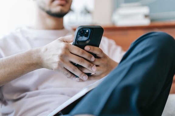 Eine sitzende Person, die ein Smartphone in ihren Händen hält.