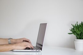 Hände tippen auf der Tastatur eines Laptops.