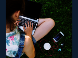 Eine Person, die ein Laptop auf dem Schoß hat und neben sich ein Smartphone liegen hat.