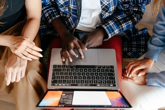 Drei Personen, die an einem Laptop sitzen.