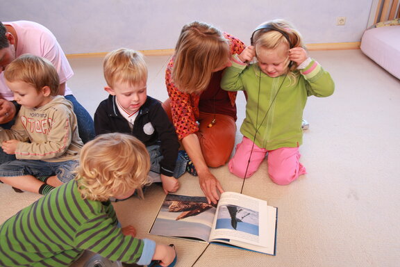 Kinder mit Kopfhörer und Fotobuch und Erzieher  