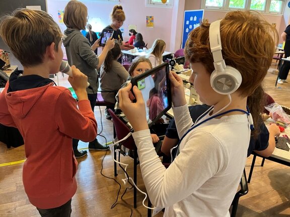 Kinder, die mit digitalen Medien wie Tablet und Kopfhörer arbeiten.