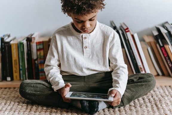 Ein Kind, das auf ein Tablet schaut, welches es in den Händen hält.