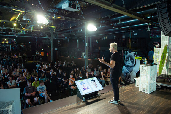 Eine Person, die auf einer Bühne steht und vor Publikum spricht.