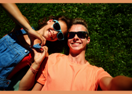Zwei junge Menschen, die auf einer Wiese liegen und ein Selfie von sich machen.