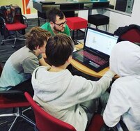 Menschen die um einen Tisch sitze, auf dem ein Laptop steht.