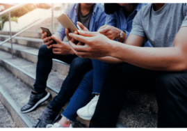Drei junge Menschen, die auf Treppenstufen nebeneinander sitzen und alle ein Smartphone in den Händen halten.