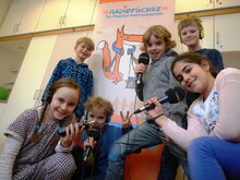 Junge Menschen, die Mikrophone und ein Aufnahmegerät in den Händen halten.