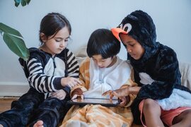 Drei Kinder, die ein Tablet vor sich liegen haben, auf dem sie spielen.