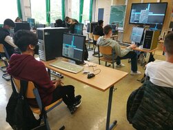 Schüler:innen, die in einem Klassenraum an PCs sitzen.