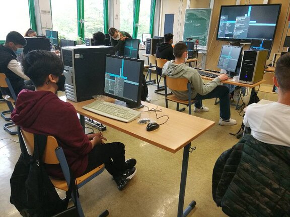 Schüler:innen, die in einem Klassenraum an PCs sitzen.