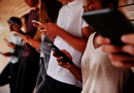 Menschen, die nebeneinander stehen und alle ein Smartphone in den Händen haben, auf das sie schauen.