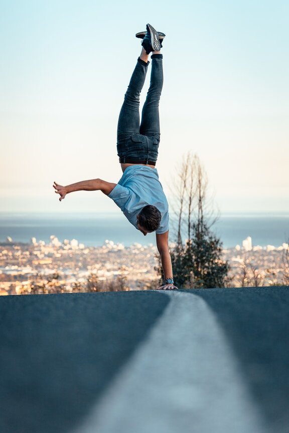 Ein Mensch, der einen einarmigen Handstand auf einer Straße macht.