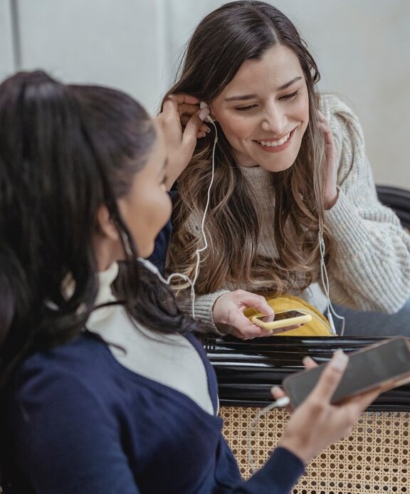Zwei Personen, die Smartphones in den Händen halten und Kopfhörer in den Ohren haben.
