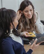 Zwei Personen, die Smartphones in den Händen halten und Kopfhörer in den Ohren haben.