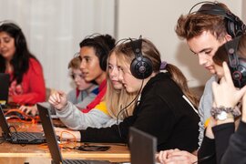 Junge Menschen, die kopfhörer aufhaben und vor Laptops sitzen.