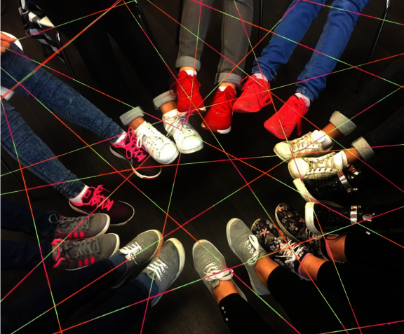 Füße mit Schuhen, die zu einem Kreis gebildet sind. Über den Füßen ist ein Netzwerk aus Bindfäden zu sehen.