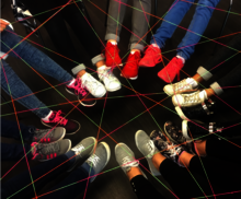 Füße mit Schuhen, die zu einem Kreis gebildet sind. Über den Füßen ist ein Netzwerk aus Bindfäden zu sehen.
