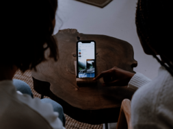 Zwei Personen, die vor einem Smartphone sitzen, welches vor ihnen auf einem Tisch steht.