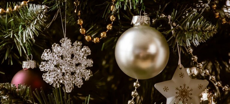 Nahaufnahme von Weihnachtsbaumschmuck. Zu sehen ist eine goldene Christbaumkugel, zwei Sterne und eine Goldkette, die an Tannenzweigen hängen