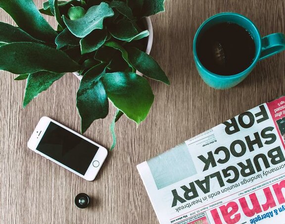 Ein Tisch mit Zeitung, Smartphone und Tasse.