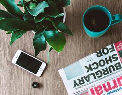 Ein Tisch mit Zeitung, Smartphone und Tasse.