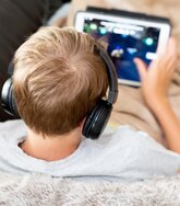 Ein Mensch, der Kopfhörer aufhat und am Tablet spielt.