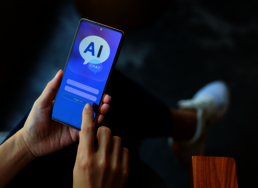 Eine Person, die ein Smartphone in den Händen hält, auf dem "AI" steht.