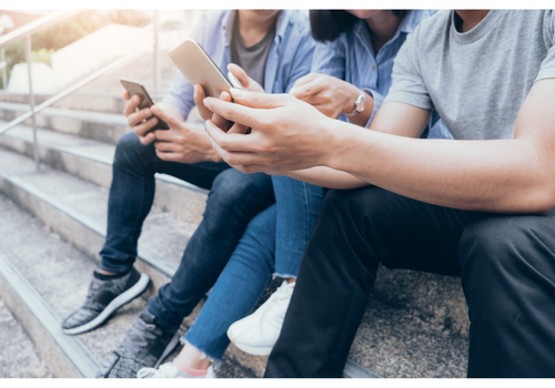 Drei junge Menschen, die auf Treppenstufen nebeneinander sitzen und alle ein Smartphone in den Händen halten.