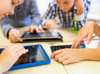 Kinder, die an einem Tisch sitzen und mit Tablets beschäftigt sind.
