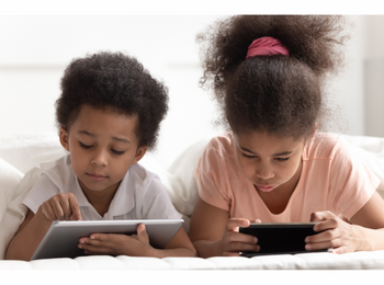 Zwei Kinder, die jeweils ein Tablet vor sich liegen haben, mit dem sie sich beschäftigen.