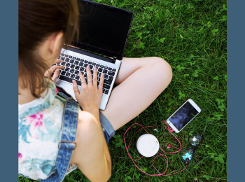 Eine Person, die ein Laptop auf dem Schoß hat und neben sich ein Smartphone liegen hat.