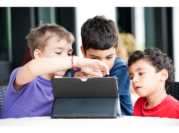 Kinder, die ein Tablet nutzen, welches vor ihnen auf einem Tisch steht.