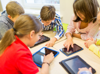 Kinder, die an Tischen sitzen, auf denen Tablets liegen.