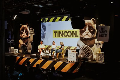 Drei Menschen, die auf einer Bühne sitzen und denen ein Publikum zuhört.