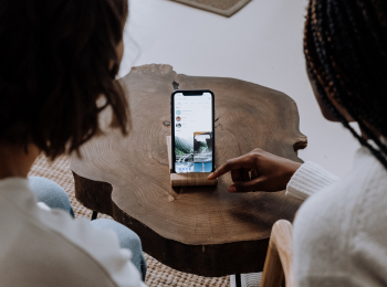 Zwei Personen, die vor einem Smartphone sitzen, welches vor ihnen auf einem Tisch steht.