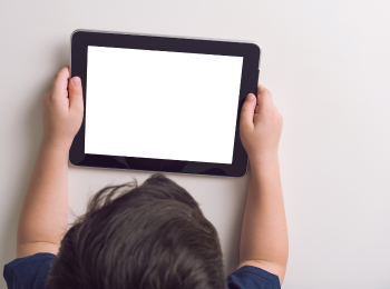 Ein Kind, das vor einem Tablet sitzt, welches es in den Händen hält.